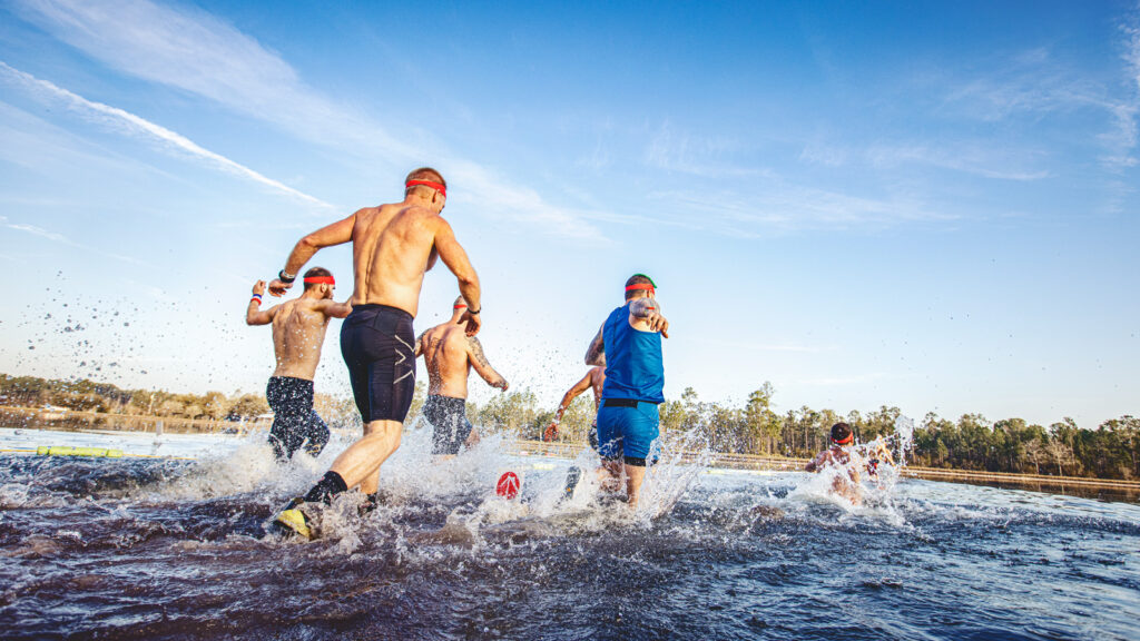 Competitors run through a body of water.