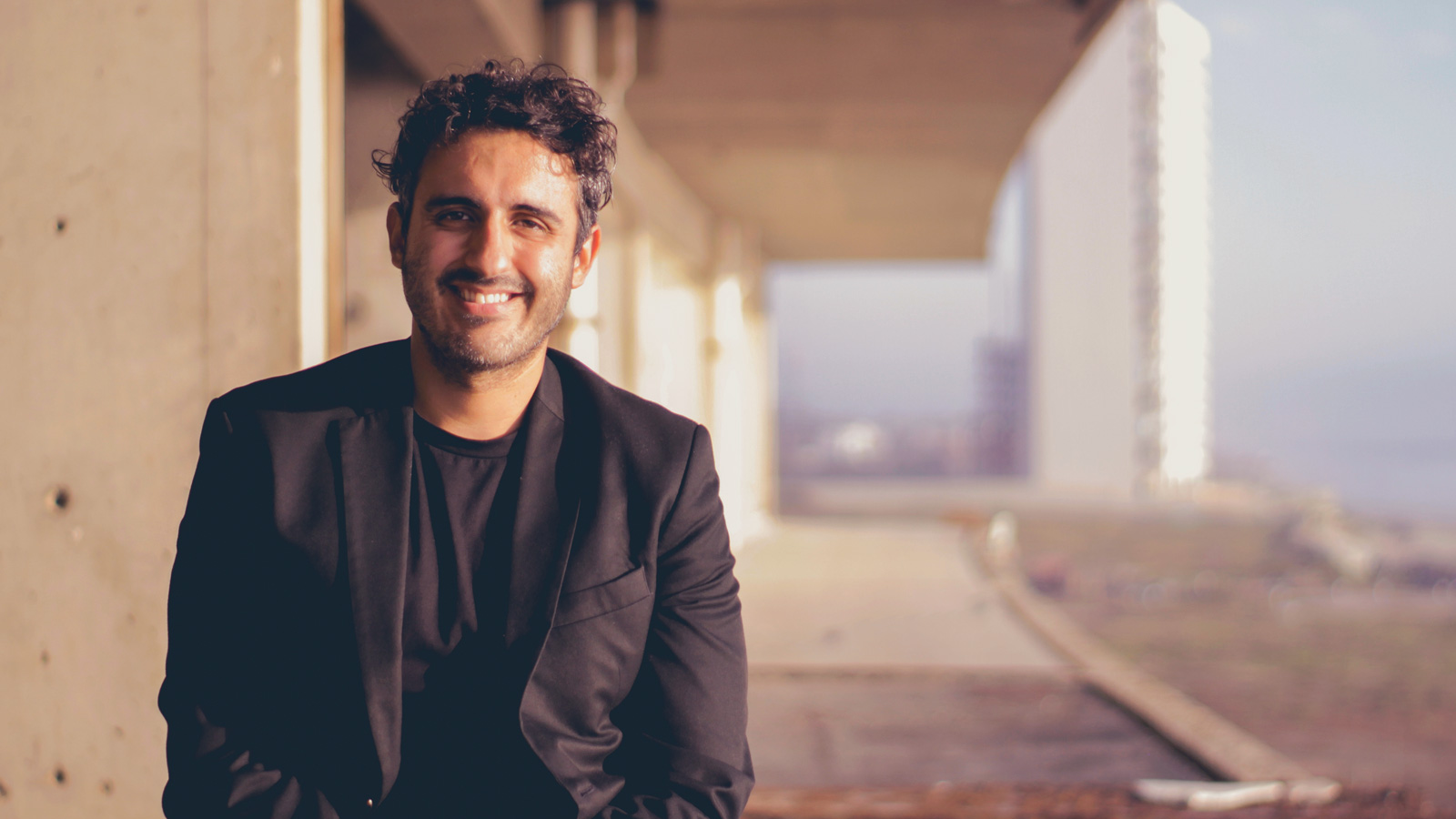 Alvaro Alvarez smiles wearing a black blazer and black shirt underneath.