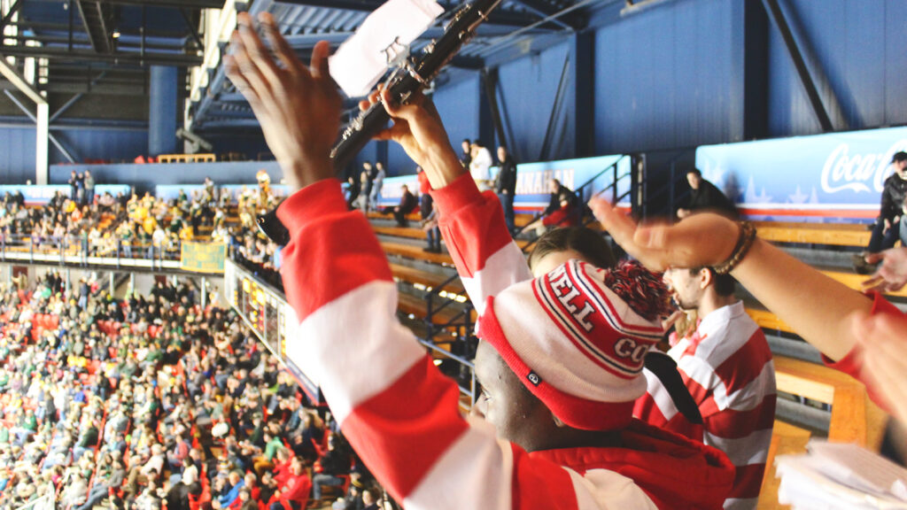 Pep Band members cheer in the foreground, with spectators in the stands in the background, during the March 2019 ECAC Championship at Lake Placid