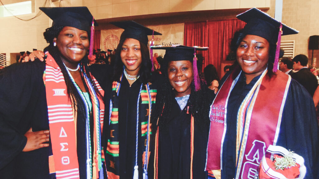 Monique Hall at graduation in regalia with friends.