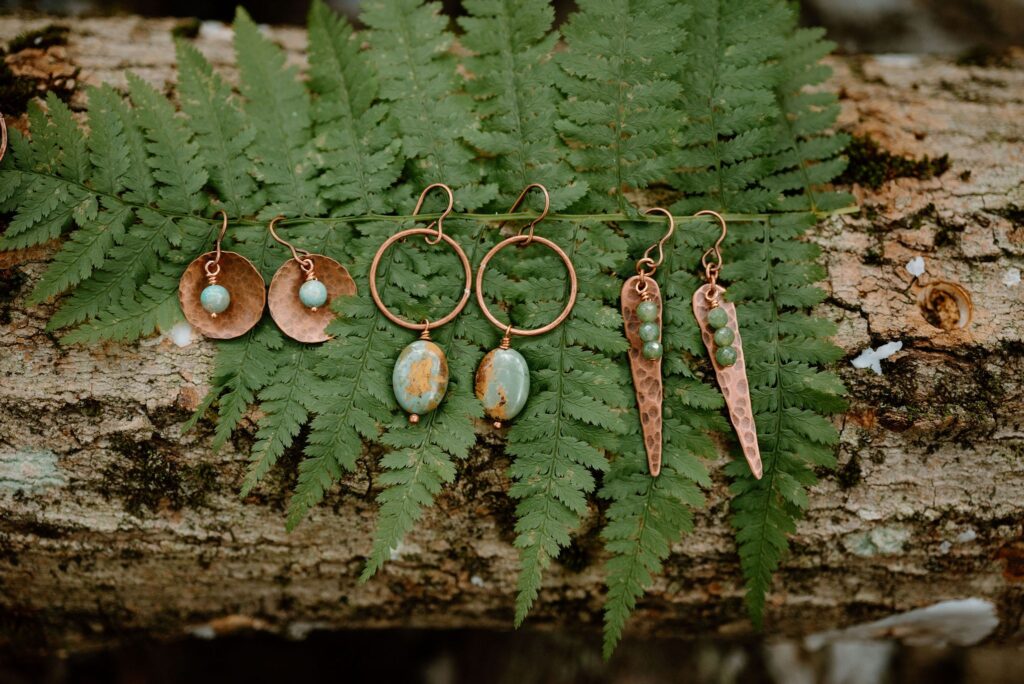 Copper and jade earrings arrayed on a fern leaf on a log