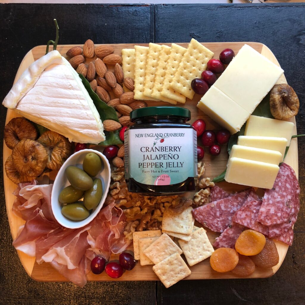A platter of charcuterie with a jar of jelly in the middle