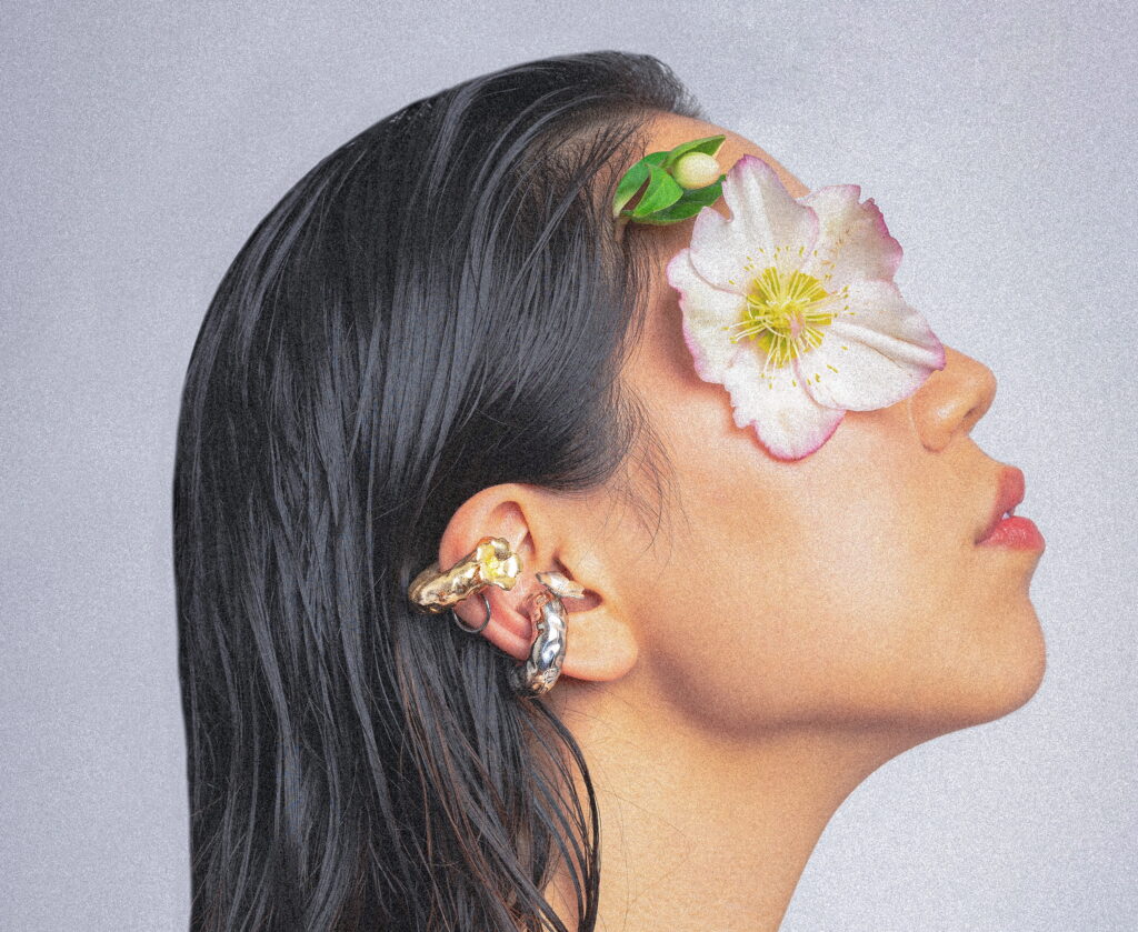 A woman in profile with a silk flower over her eye wearing earrings