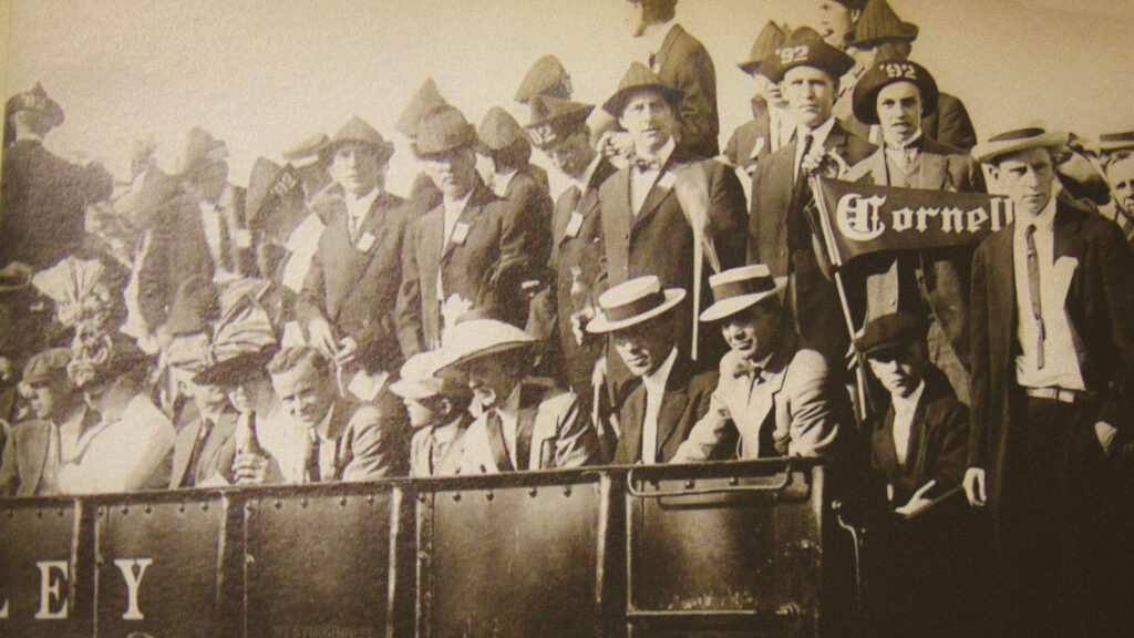 a photo showing spectators on an observation train preparing to watch a crew race; a Cornell pennant is seen in the crowd