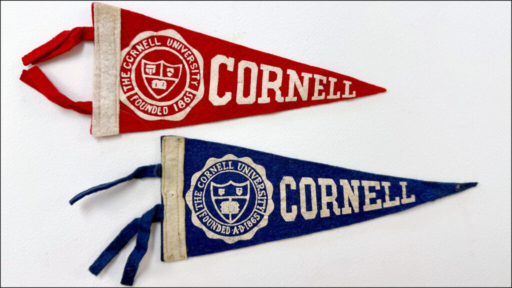 two small (9-inch) vintage Cornell pennants, one red and one blue, on a white background