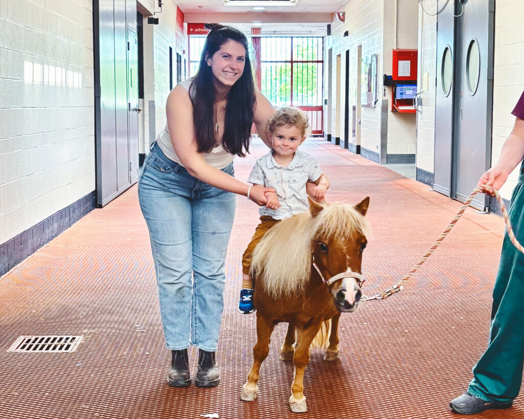 A little boy rides on Minnie as a woman holds him.