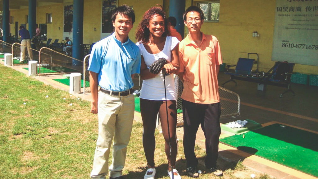Troy Mullins holds a golf club at the driving range and smiles with two friends in Beijing.