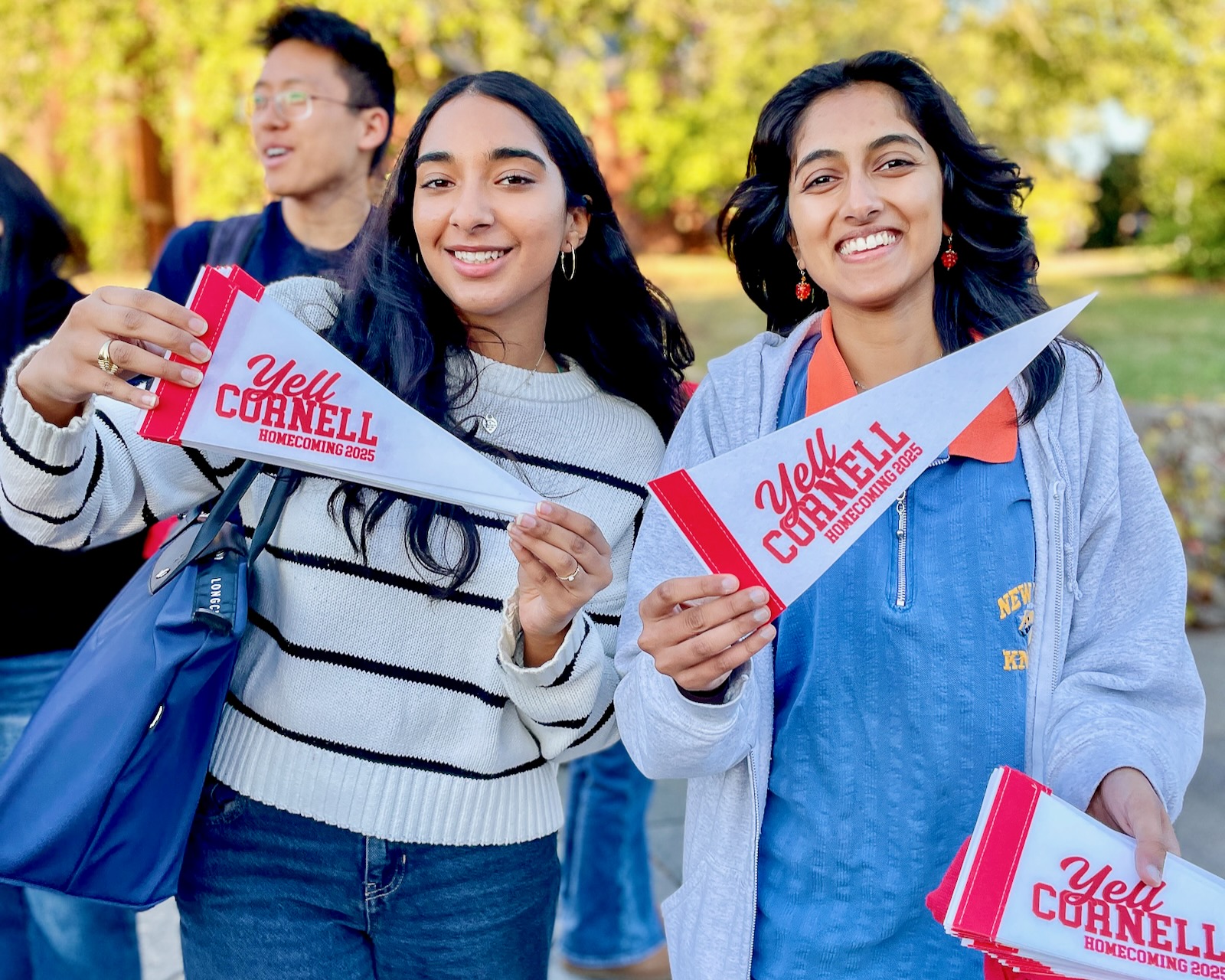 Two female students hold pennants that say 'Yell Cornell: Homecoming 2025"