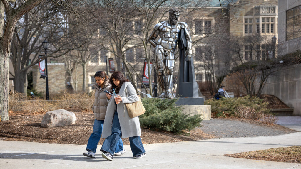 two students cross between Statler and Uris halls with the "Herakles" statue behind them on the first day of classes
