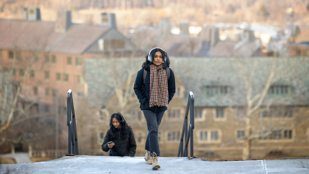 A student wearing a coat, scarf, and pair of headphones reaches the top of the Slope from West Campus on the first day of classes