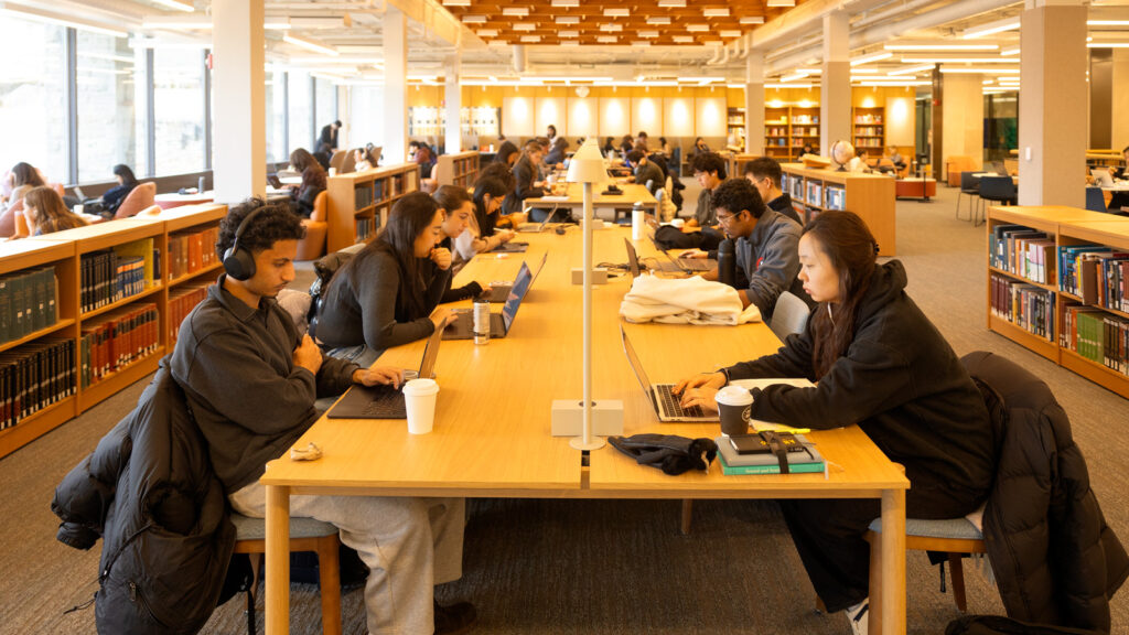 Dozens of students sit at tables in Olin Library using their laptops.