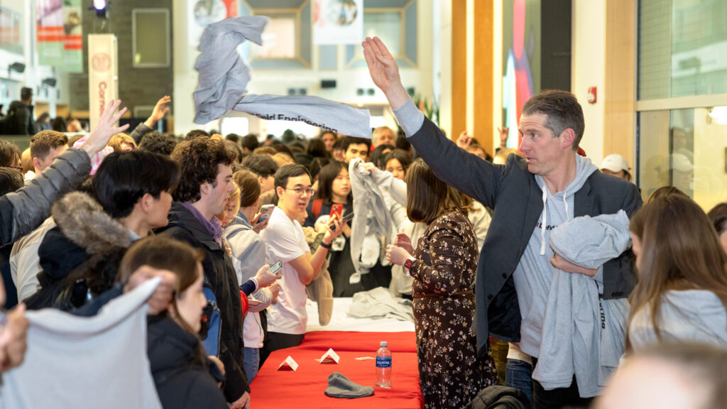 A man throws gray apparel branded with Cornell Duffield Engineering during the naming celebration in Duffield Hall.