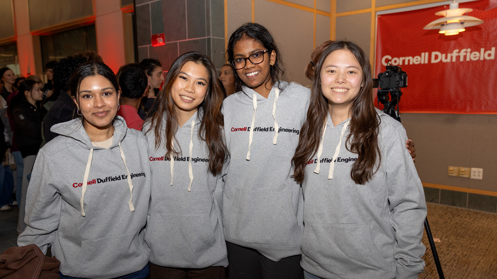 Four students smile for a photo wearing gray sweatshirts that say Cornell Duffield Engineering.