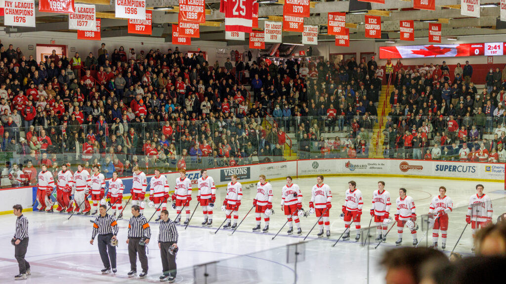 Cornell hockey players stand in a line on the ice during the Canadian national anthem.