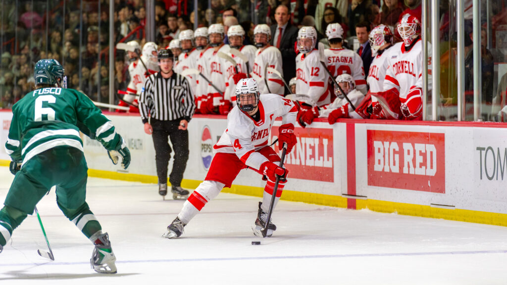 A Cornell men's hockey player skates down the ice with a Dartmouth defender to his side.
