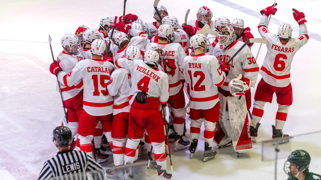 The Cornell men's hockey team in their uniforms in a group huddle on the ice.