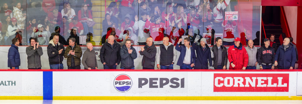 A line of fans next to the ice clap as fans in the stands cheer behind the glass at Lynah Rink.