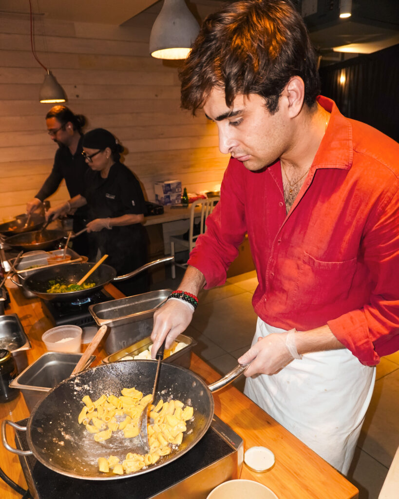 Maximo Mander in action moving a pan of hot pasta around with a spatula.