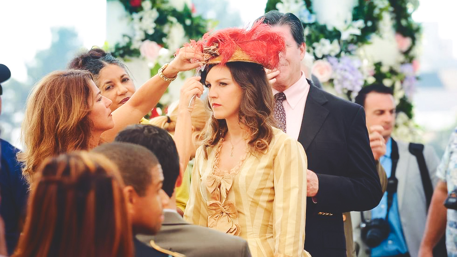 Carla Gallo on set as two women fix her hat.