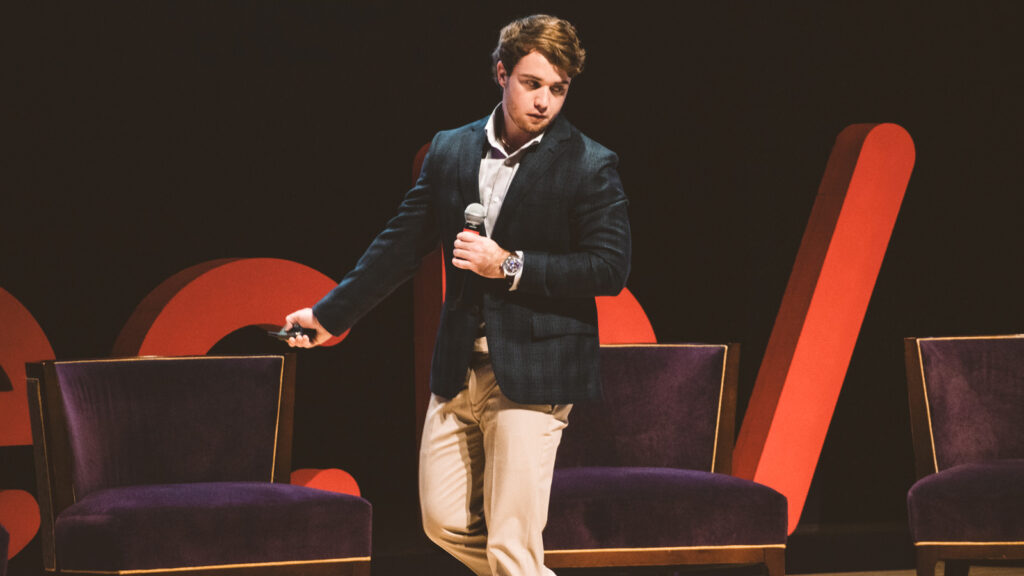 Will Conway walking on stage presenting with a microphone in his hand.