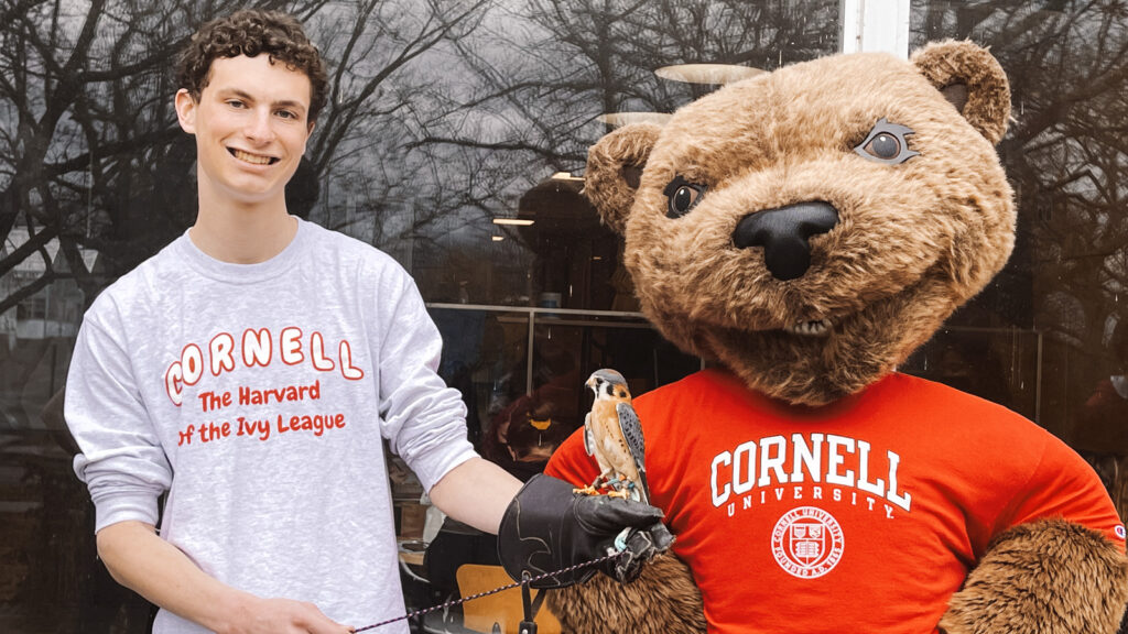 A student handler smiling with one of the raptors and Touchdown.