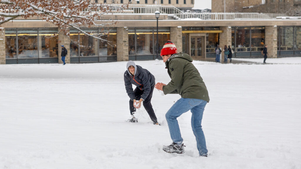 Two male students have a snowball fight outside Olin Library