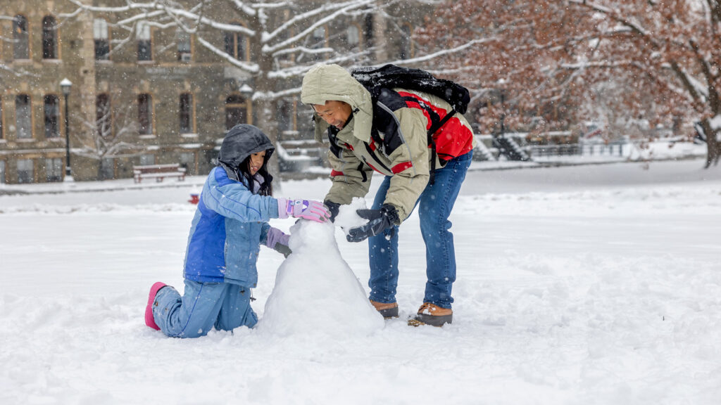 A man and child making a snowman on the arts quad