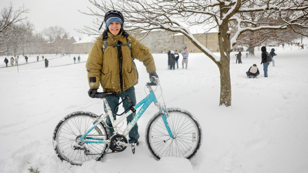 A student stands with his bike on a snowy Arts Quad