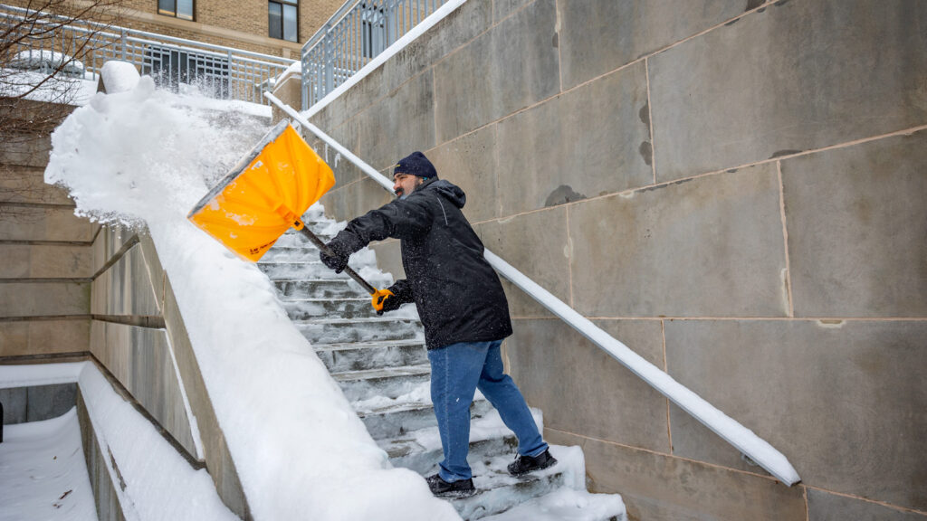 A man shovels snow on a staircase on the Ag Quad