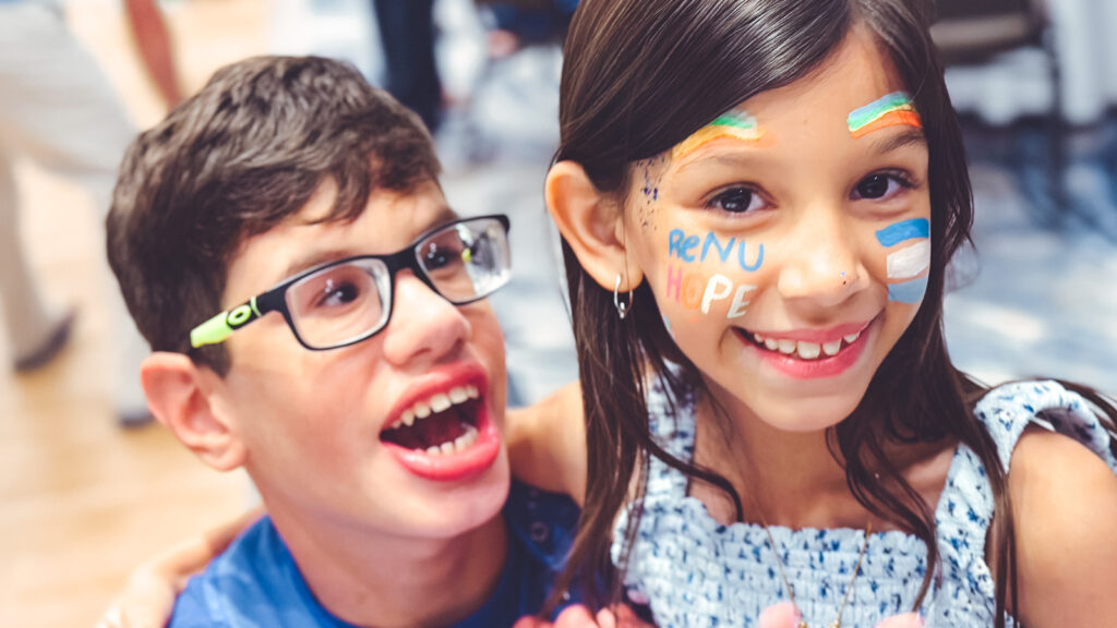 Devon and sister Violet smile for a photo. Violet is wearing face paint that says "ReNU Hope."