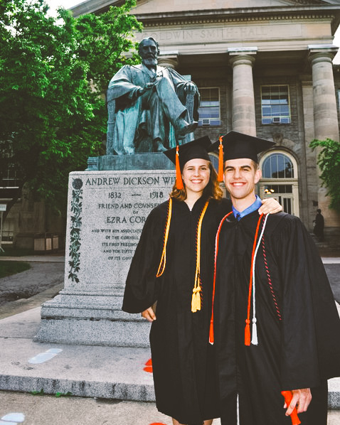 Adam Mangano Drenkard ’11 & Lauren Mangano Drenkard in caps and gowns in front of the Ezra statue