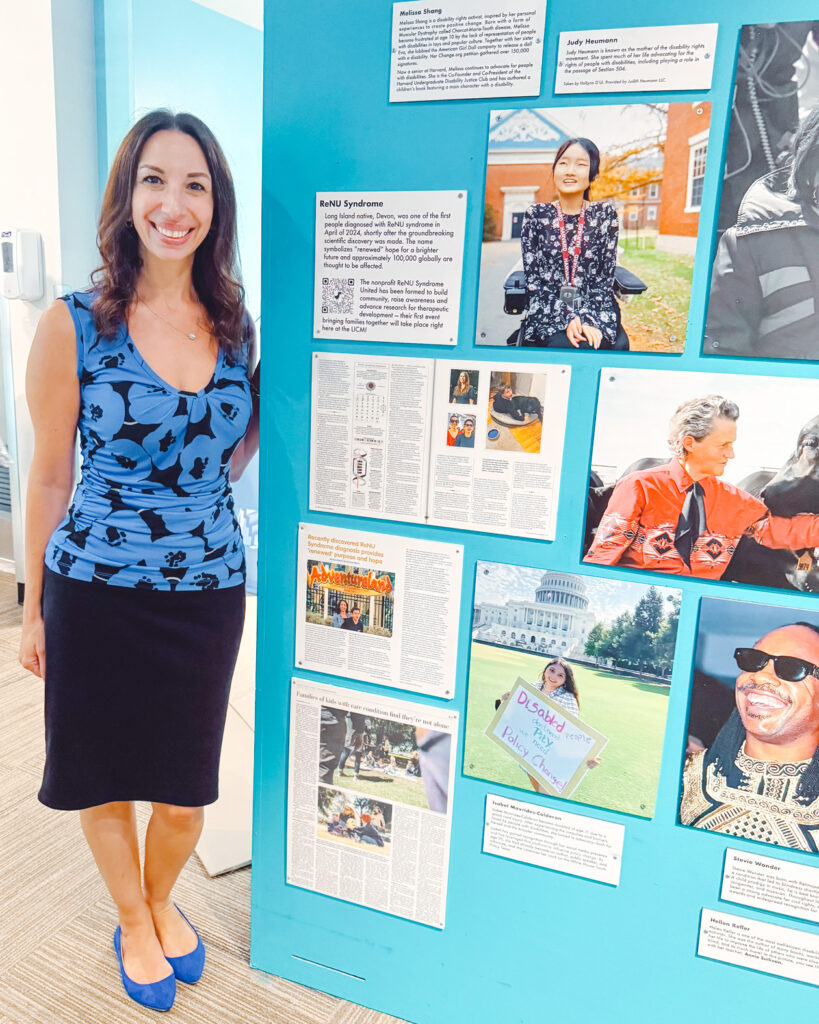Jessica Margrill in a blue, patterned blouse and skirt standing next to an exhibit for ReNU Syndrome at the Long Island Children's Museum.