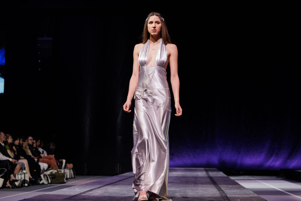 A model walks down the runway in a long, silver silk dress with beading and matching beaded headpiece.