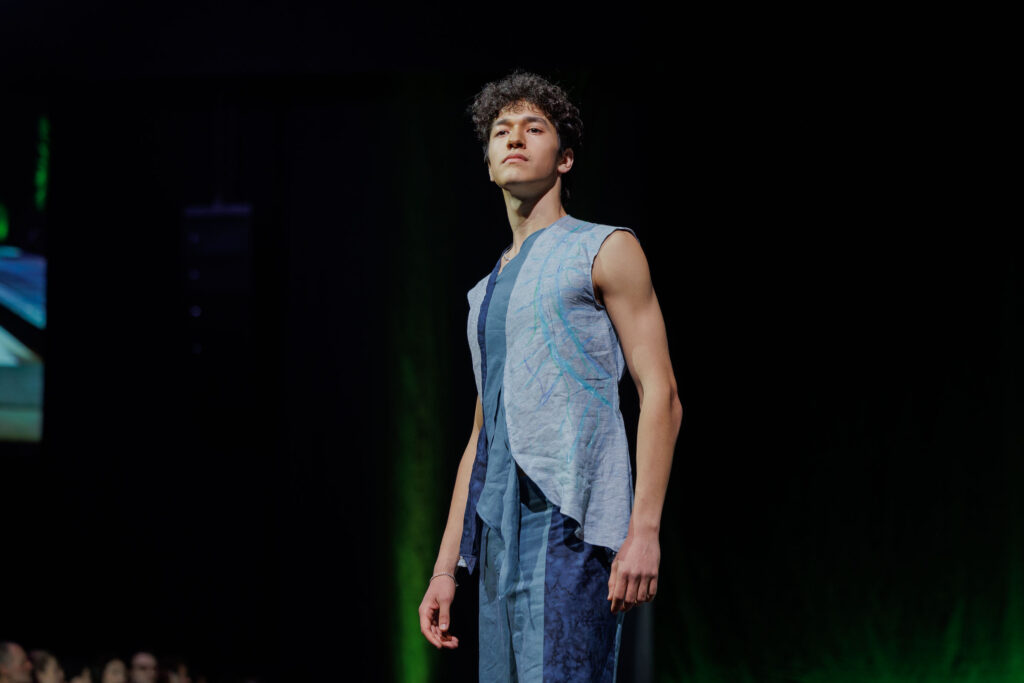 A student poses on the runway wearing matching tank top and pants featuring thick lines of blues throughout.