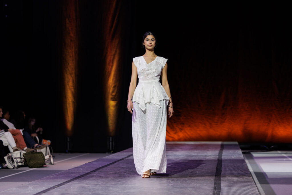 A student walks down the runway wearing a flowy white blouse and pants.
