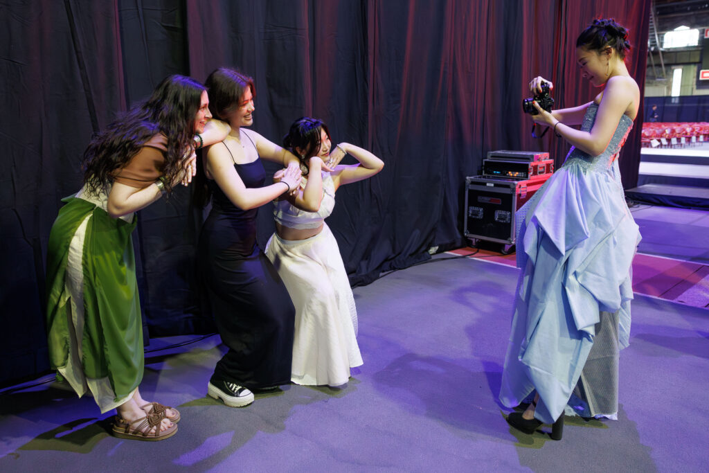 A student in a blue dress takes a photo of three other students posing together.