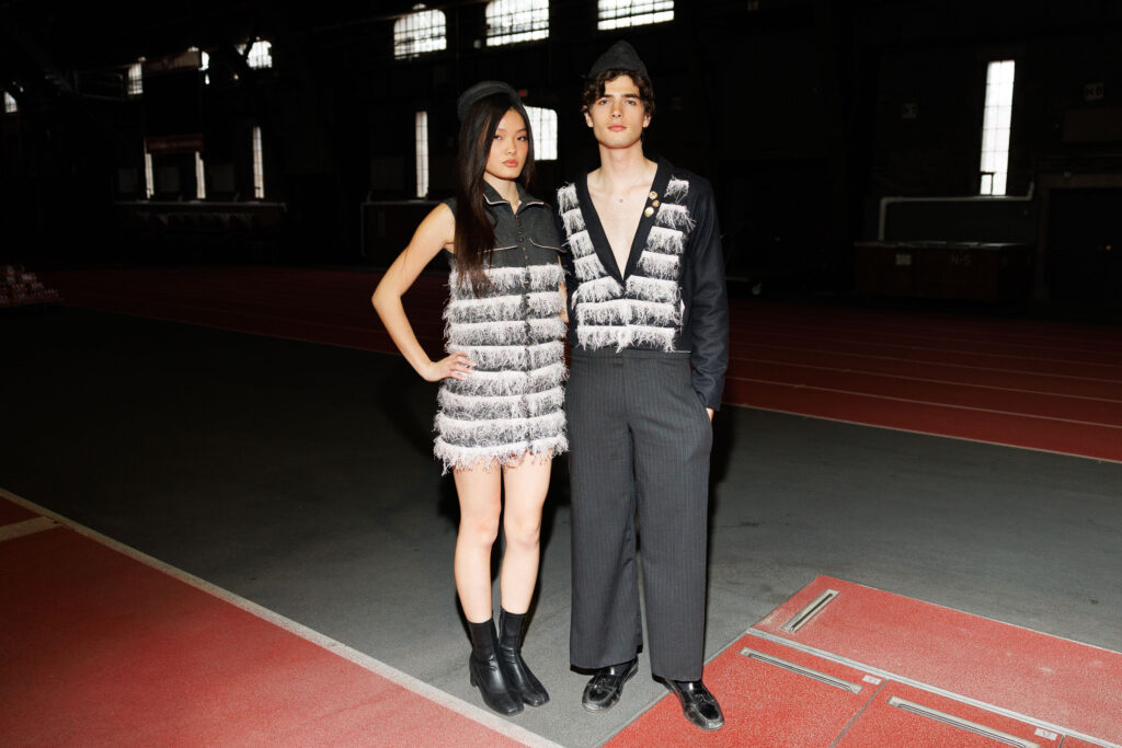 Two students wearing black with white tassel accents and black hats pose together for a photo
