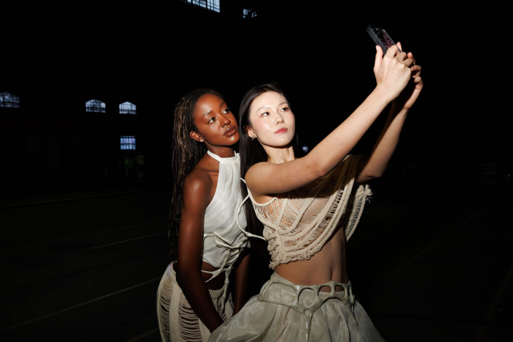 Two students wearing cream and white tops and skirts pose for a selfie together