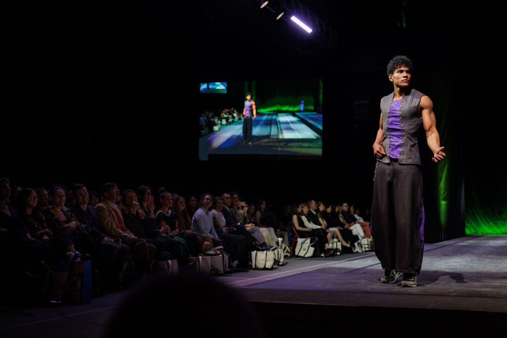 A student wearing a black vest and purple shirt strikes a pose at the end of the runway