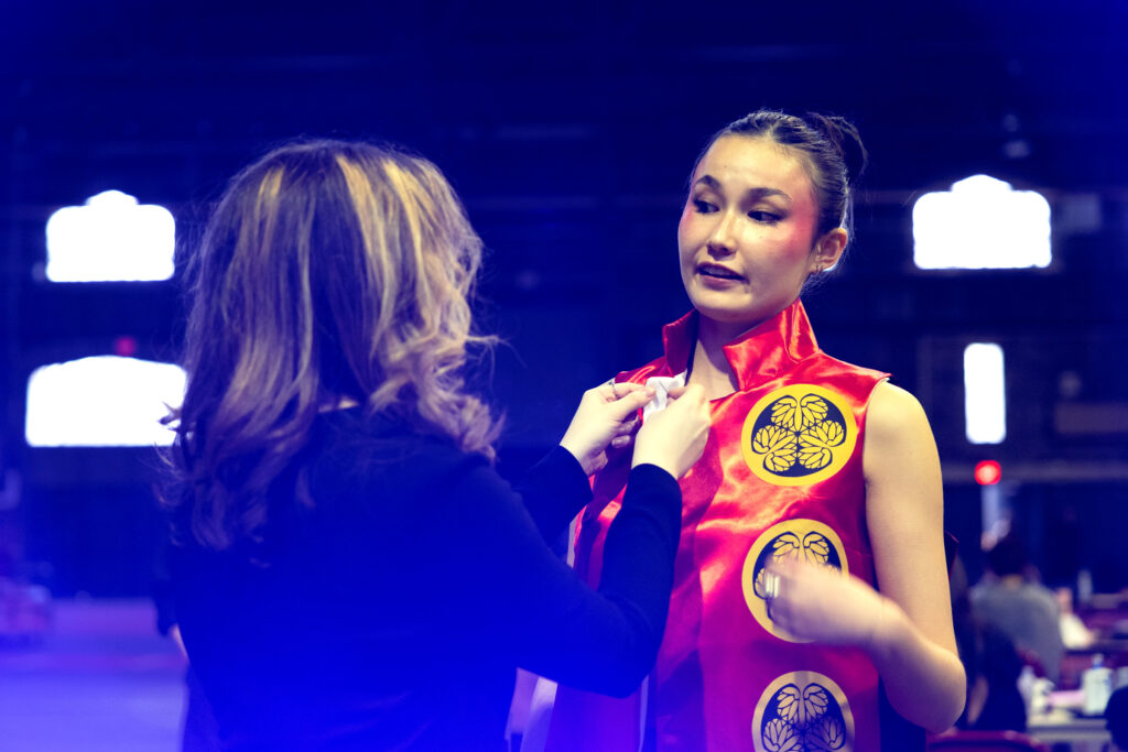 Two students talk to each other while one makes adjustments to the collar of the runway outfit.