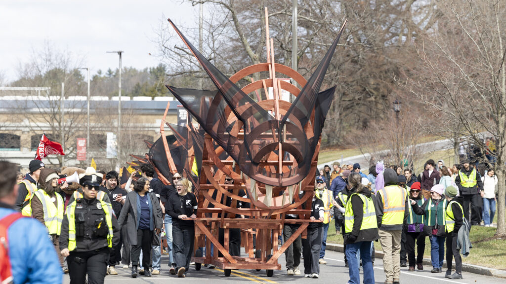 The front of the orange, wooden dragon with black mesh as it is paraded down the street during Dragon Day 2026