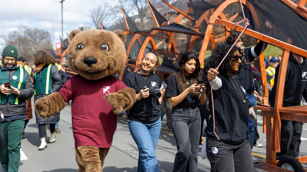 Touchdown, wearing a Dragon Day shirt, walks next to students and the dragon during the parade