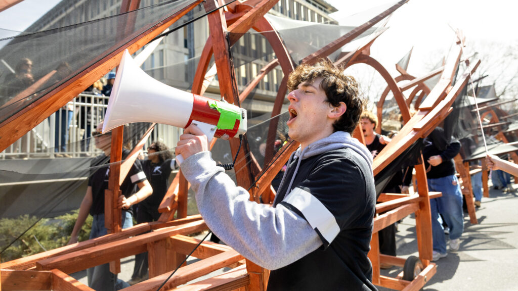 A student yells into a megaphone while walking next to the dragon as it arrives on the Arts Quad during Dragon Day 2026