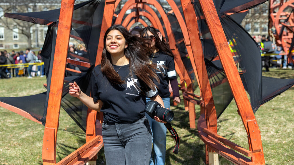 A student holding a camera smiles and walks underneath the dragon during Dragon Day 2026