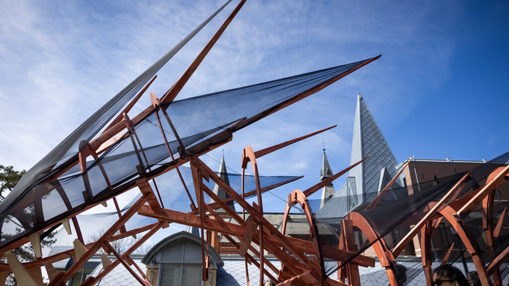 The top of the dragon for Dragon Day 2026, featuring an orange, wooden body with black mesh, with the spires of Sage Hall visible in the background