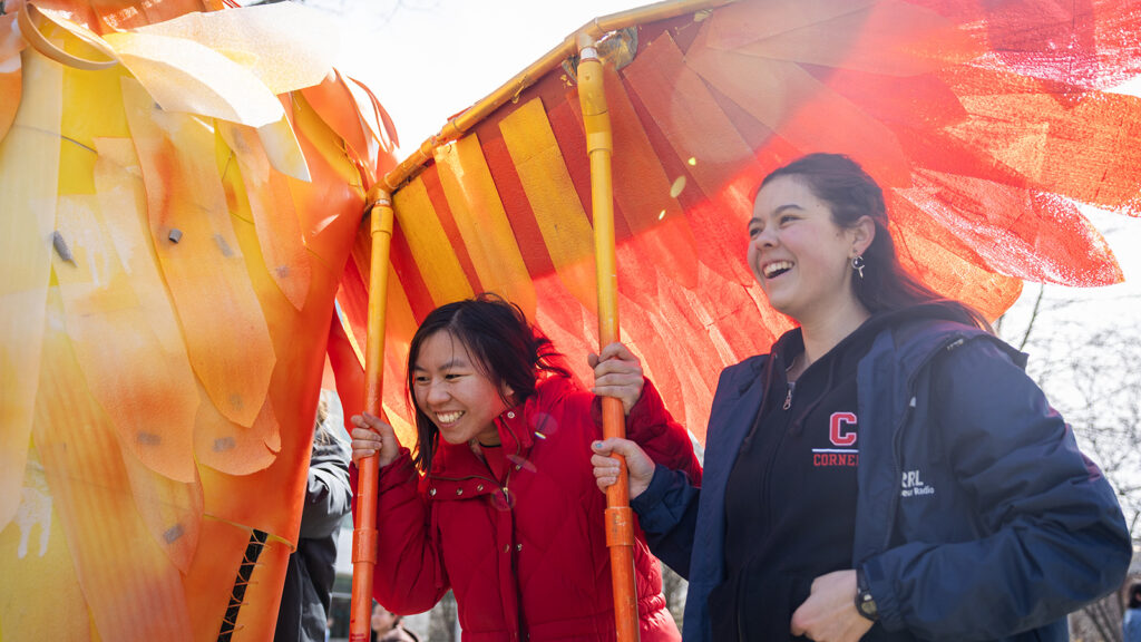 Two smiling students hold the wing of the phoenix at Dragon Day 2026