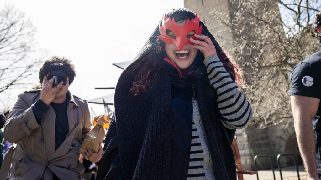 A smiling student holds a red dragon mask on her face