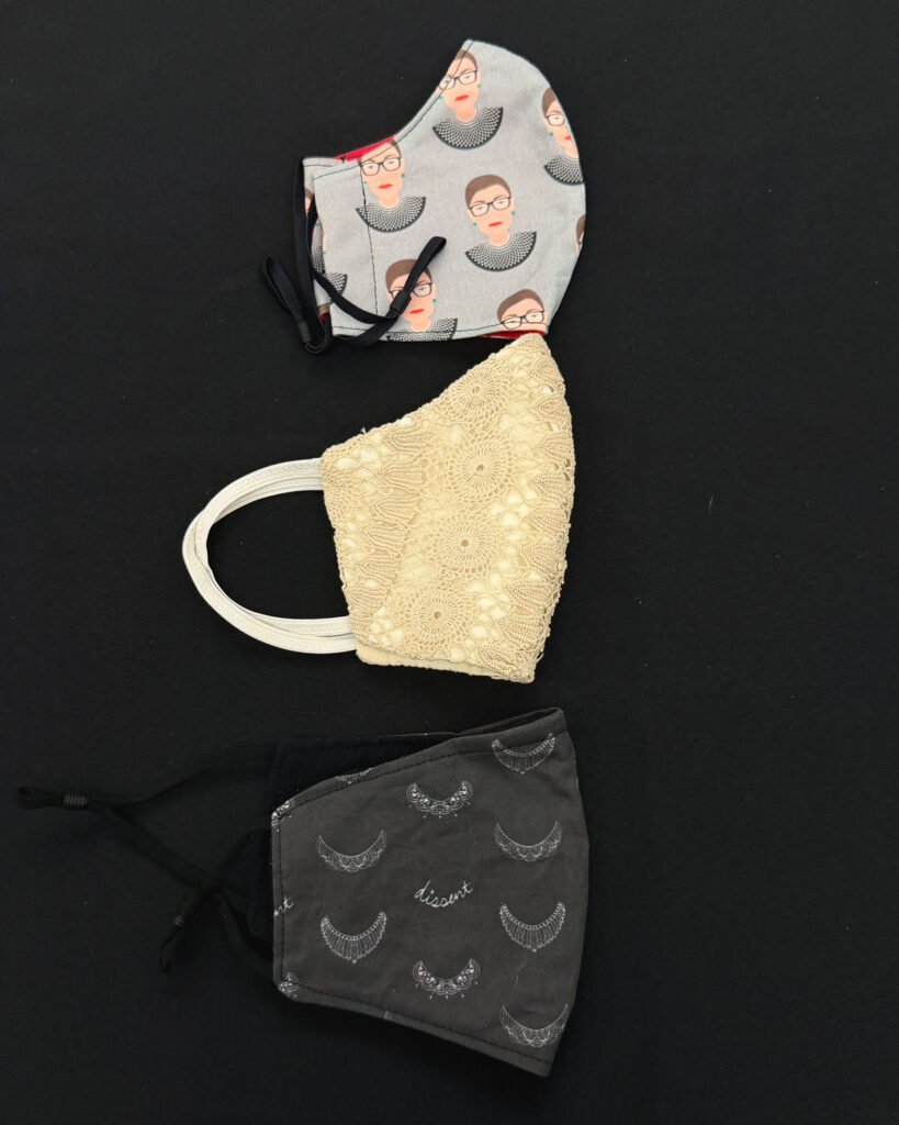 Three covid face masks. One has an RBG design, one is gold and embroidered, one is black with judicial collar designs.