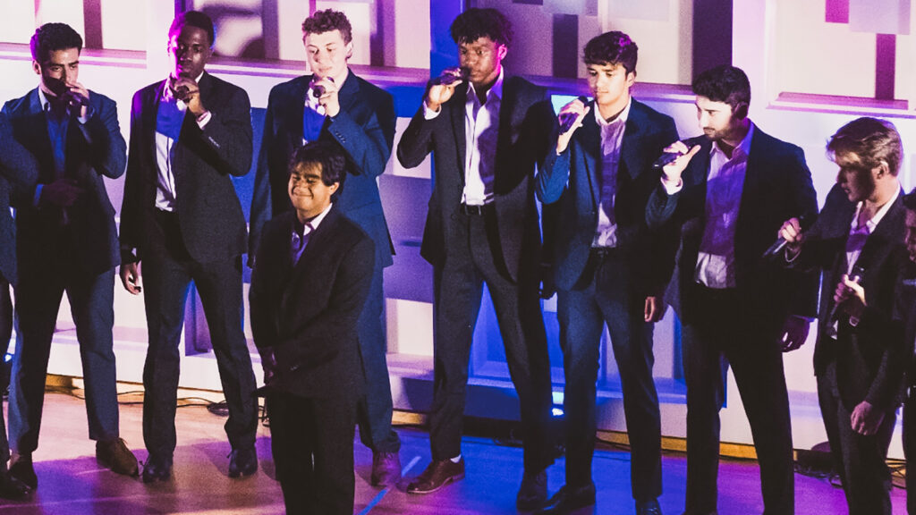 Adi Arora with seven of his classmates singing during an a cappella performance on stage.