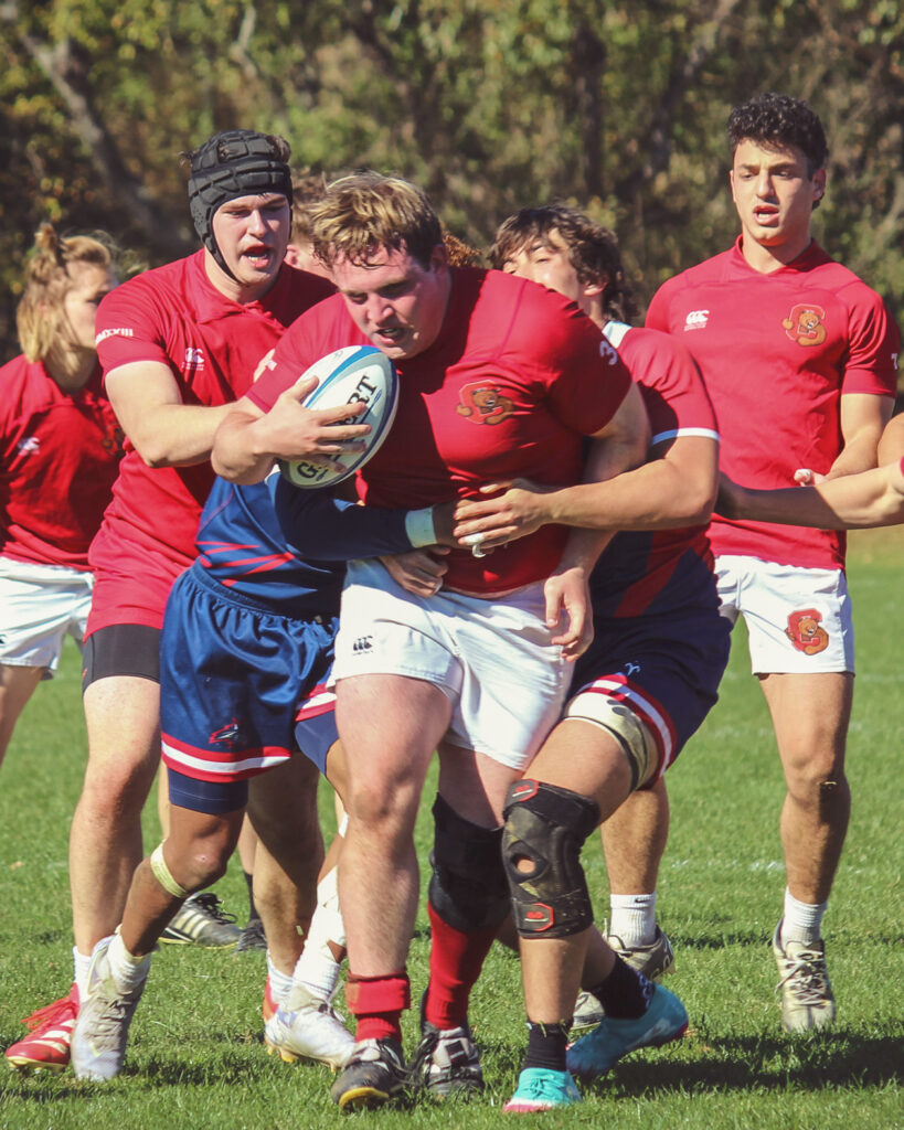 Matthew Lane pushes through opponents with the ball while they try to hold him back.